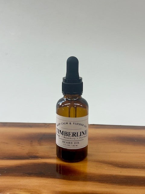 A small amber glass dropper bottle labeled 'TIMBERLINE Beard Oil' sits on a wooden surface against a plain light gray background.