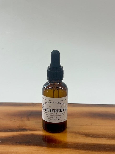 A small amber glass dropper bottle labeled 'Bearded Oil' by Blue Calm & Flicker Co., standing on a wooden surface against a plain light background.